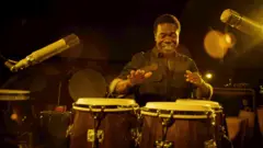 Paulinho da Costa tocando um instrumento durante gravações do documentário
