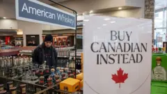 Um homem em uma loja de bebidas onde tem uma placa pedindo que se comprem produtos canadenses.