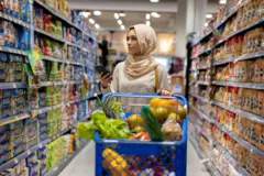 سيدة مسلمة في محل سوبر ماركت وبيدها هاتف محمول