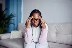 Aworan obinrin kan to joko pẹlu awo oju loju rẹ, o fi ọwọ mejeeji di ori mu