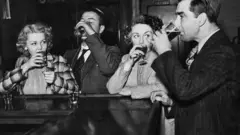 Uma foto em preto e branco de pessoas bebendo em um bar.
