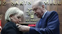 Erdoğan geride AK Parti yazan kürsünün önünde Özemir'e rozet takıyor.