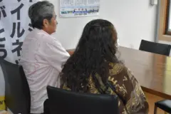 Duas pessoas de costas sentadas diante de mesa em sala