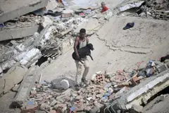 Um homem carrega um cachorro preto resgatado dos escombros de um edifício que desabou após dois terremotos em Caraballeda, no estado de La Guaira, cerca de 40 km a nordeste de Caracas, em 25 de junho de 2026.