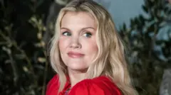 Emerald Fennell olha por cima do ombro na estreia de *Wuthering Heights* em Londres; ela tem longos cabelos loiros.