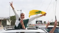 Lübnanlılar ateşkesi kutluyor. Beyaz başörtülü bir kadın arabanın üst camından dışarı çıkmış bir halde ve bir elinde Lübnan bayrağı bir eliyle barış işareti yaparak kameraya bakıyor, araçtan barış işareti yapan başka eller de uzanmış