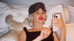 دون کلی، سازنده محتوا، در رختخواب دراز کشیده و دور تا دورش را بالشت‌ها احاطه کرده‌اند، کلاهی ابریشمی به سر دارد، چشم بند وبرچسب دهان مخصوص خوابیدن دارد، تلفن همراه را در دست گرفته است