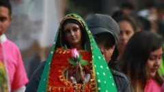 Una mujer con un gorro negro sostiene una efigie de la Virgen de Guadalupe