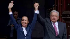 Presidente e ex-presidente do México com as mãos levantadas em saudação.