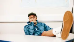 Ben Hurst, um homem negro, de casaco e com as pernas estendidas em uma mesa