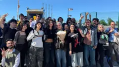 Ortada elinde çiçekle Hafize Çetin, etrafında arkadaşları duruyor.
