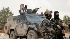 Güvenlik güçleri, 9 Şubat 2026'da Suriye'nin kuzeydoğusundaki Haseke kırsalında düzenlenen ortak ziyaret sırasında zırhlı bir aracın önünde duruyor