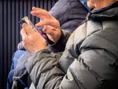 Idosa manuseia smartphone e é fotografada em ângulo lateral, sem mostrar o rosto