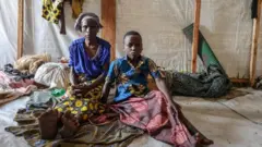 Angela N'Habimana w'imyaka 67, n'umwuzukuru we bari mu kigo rusange i Kiwanja muri Rutshuru, nyuma y'uko aho batuye habereye imirwano