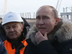 Vladimir Putin com a mao esquerda no queixo em frente a ponte na Crimeia