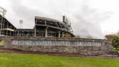 Uma placa com os dizeres "Universidade Estadual da Pensilvânia" em uma parede de concreto do lado de fora do estádio de atletismo da universidade.