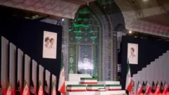 Caixões cobertos com a bandeira iraniana descansam sobre uma plataforma ladeada por bandeiras e retratos dos aiatolás