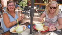 Duas mulheres estão sentadas em um restaurante com margaritas e enchiladas em cima da mesa