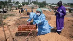 Amatsinda y'abakozi bo mu muryango wa Croix-Rouge na Croissant-Rouge bategura aho gushyingura, mu irimbi rya Mbiyo, imfubyi ya kane yishwe na Ebola, yo mu kigo cy'imfubyi cy'i Bunia, mu ntara ya Ituri, muri Repubulika ya Demokarasi ya Congo. Ifoto yo ku itariki ya 19 Kamena (6) mu mwaka wa 2026.