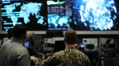 Two us cyber command officers in front of giant screens with data and information on them