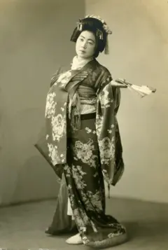 Mulher japonesa vestida com quimono, com flores e leque em uma das mãos