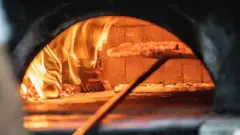 Uma pizza sendo colocada no forno