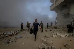 مجموعة من الأشخاص يحاولون النجاة من القصف الإسرائيلي، يركضون وسط أبنية مدمرة وداخن كثيف ناجم عن القصف الإسرائيلي على مدينة غزة.