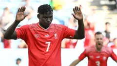Breel Embolo dari Swiss, mengenakan kaus merah bernomor tujuh, mengangkat tangannya setelah mencetak gol melawan Kamerun, negara kelahirannya, di Piala Dunia 2022
