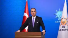 Ömer Çelik yanında AKP bayrağı olan kürsüde açıklama yaparken 