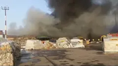 পলিথিনে ঢেকে রাখা কিছু মালামাল, পেছনে কালো ধোঁয়া উড়ছে 