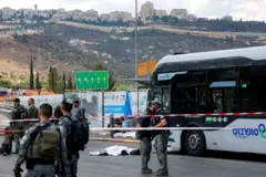 Olay yeri. Polis kordonu. Güvenlik görevlileri ve arkalarında ateş açılan otobüs durağı. 