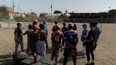 Niños escuchan a un profesor de Beisbol.