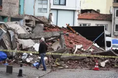 depremde yıkılmış etrafı çevrili bir bina ve önünden geçen bir adam