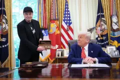 Elon Musk de pé sorrindo apontando para Donald Trump que está sentado, durante reunião no Salão Oval da Casa Branca