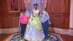 Uma mulher de camisa listrada azul, com o rosto borrado, posa ao lado de uma funcionária da Disney de vestido amarelo. A filha, também com o rosto borrado, aparece do outro lado, usando tiara do Mickey e camiseta rosa.