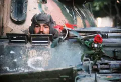 جندي يطل رأسه من فوهة دبابة وبجانبه وردة حمراء معلقة