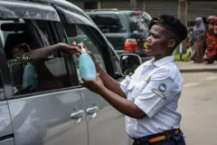 Um agente de segurança fornecendo água clorada ao passageiro de um carro no Hospital Nacional Muhimbili em Dar es Salaam, na Tanzânia, poucas horas após o governo anunciar o primeiro caso de covid-19 no país em 16 de março de 2020