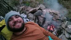 Homem deitado e sorrindo, deitado ao lado de fogueira