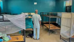 Čovek stoji leđima okrenut kameri u spavaonici sa krevetima u internatu Svete Marije u selu Papiri u državi Niger