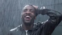 Young man dey stand inside rain, as e dey look up