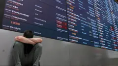 Табло в аэропорту и усталый человек на корточках