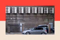 れんが造りの建物の上部に、エアコンの室外機が並べて設置されている。建物の前には複数の自動車が停まっている