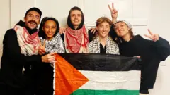 "Los 5 de Ulm" incluyen a (de izquierda a derecha) Daniel Tatlow-Devally, Zo Hailu, Crow Tricks, Vi Kovarbasic y Leandra Rollo. Aparecen en la foto con una bandera palestina.