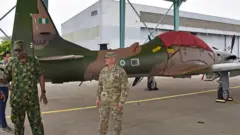 One US Military officer and im Nigeria counterpart stand close to a military aircraft for hanger