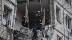 Несколько спасателей работают в разрушенной квартире в многоэтажном доме.