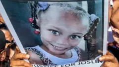 Someone in a crowd holds up a poster of Joshlin Smith with the words underneath her image saying, 'Justice for Joslin (sic)'.