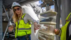 Michelle Peters (po lewej), kierowniczka ds. technicznych i zgodności w Poseidon Water, oraz Jessica Jones, dyrektor ds. komunikacji w Poseidon Water (niewidoczna na zdjęciu), trzymają model zbiorników filtracyjnych z warstwami antracytu, piasku i żwiru, które pomagają eliminować glony, materiały organiczne i inne cząstki w sekcji wstępnego oczyszczania w zakładzie odsalania wody w Carlsbadzie 