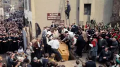 O momento em que Mick Meany foi retirado do caixão, com muitas pessoas à sua volta