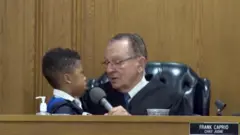 Judge Frank Caprio wearing a gown and sitting in court with a child next to him in the presiding chair