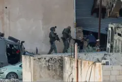 عنصران من القوات الإسرائيلية بزي عسكري يحملان السلاح، أثناء عملية جنين في الضفة الغربية المحتلة، يوجهان السلاح نحو شابين فلسطينيين يرتديان لباساً مدنياً. الصورة التقطت نهاراً.